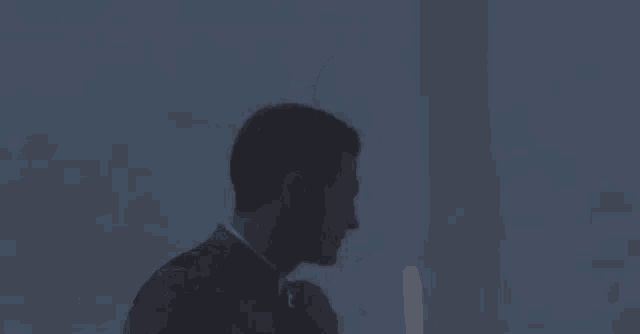 a man in a suit and tie is standing in a dark room holding his hand to his chest .