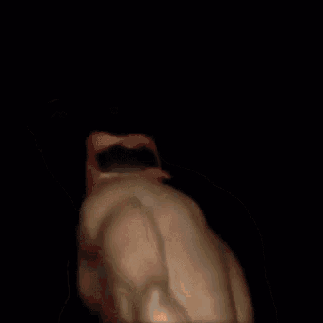 a shirtless man wearing a red hat is dancing in the dark .