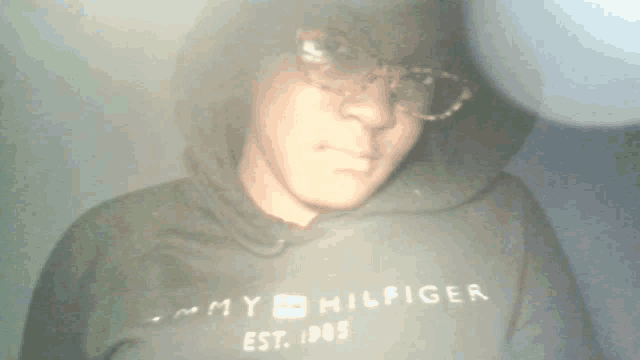 a man wearing a black tommy hilfiger hoodie and glasses