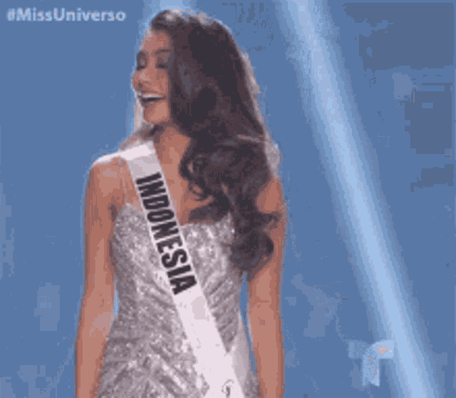 a woman in a silver dress with a sash that says indonesia is smiling .