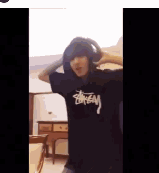 a person wearing headphones and a stussy t-shirt is dancing in a room .