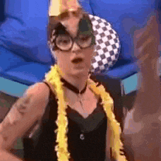 a woman wearing glasses and a yellow lei is standing in front of a couch .
