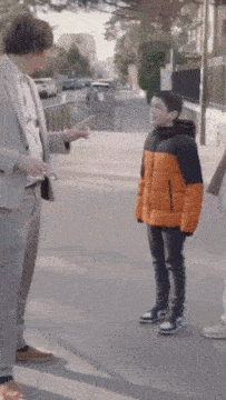 a man in a suit is pointing at a boy in an orange coat