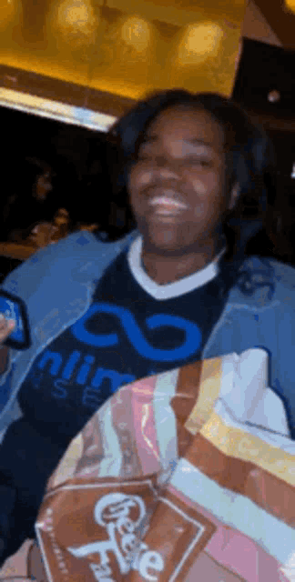 a woman wearing a shirt that says infinity smiles while holding a bag of chocolate chip cookies