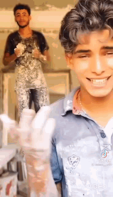 a man is smiling while another man is standing behind him covered in paint .