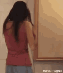 a woman in a red tank top looks at herself in the mirror