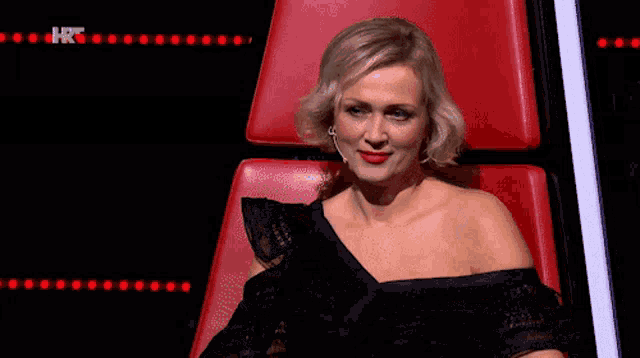 a woman in a black dress is sitting in a red chair with hrt written on the bottom