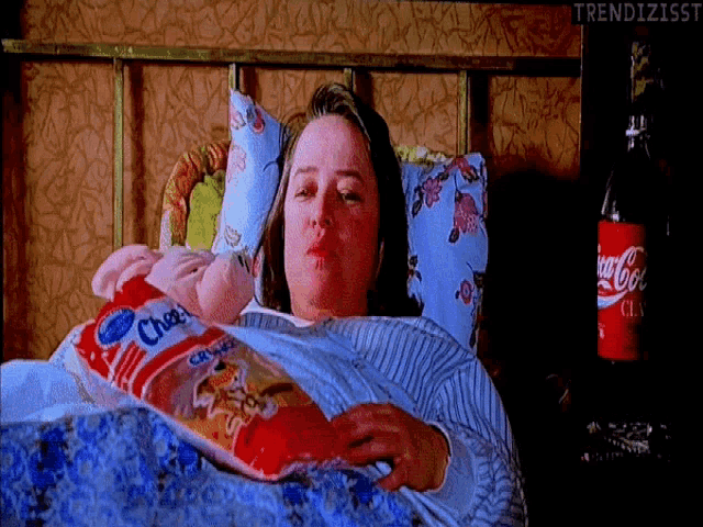 a woman is laying in bed with a bag of cheetos and a coca cola bottle