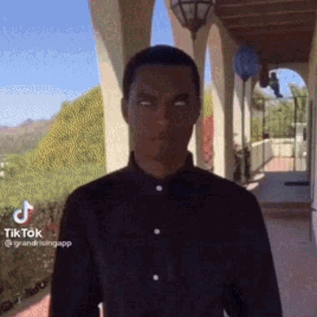 a man in a black shirt is standing on a porch with his eyes closed and a tiktok logo on the bottom right