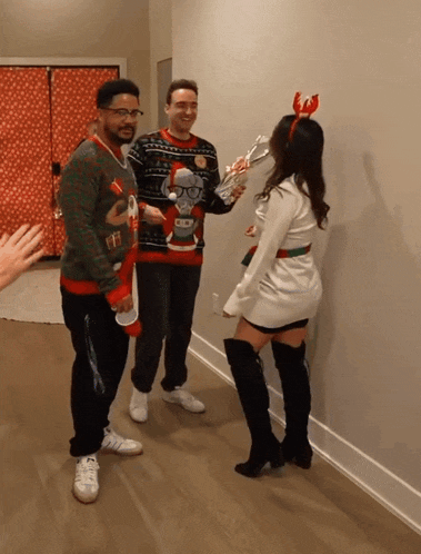 a woman in a reindeer headband stands next to two men in ugly christmas sweaters