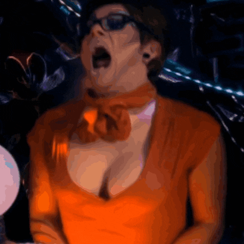 a woman in an orange top and scarf is screaming with her mouth wide open