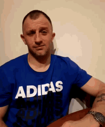 a man wearing a blue adidas shirt looks at the camera