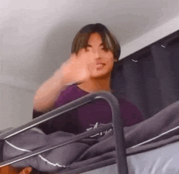 a young man is sitting on top of a bunk bed waving his hand .