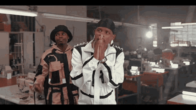 two men are standing in a room with their hands folded in front of their faces