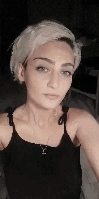 a woman with short blonde hair is wearing a black tank top and a necklace with a cross .