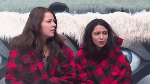 two women wearing plaid shirts are sitting next to each other in front of a painting of an eye .