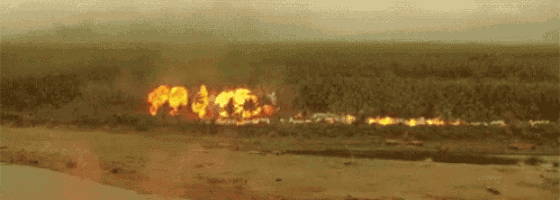 a large fire is burning in the middle of a field with a river in the foreground