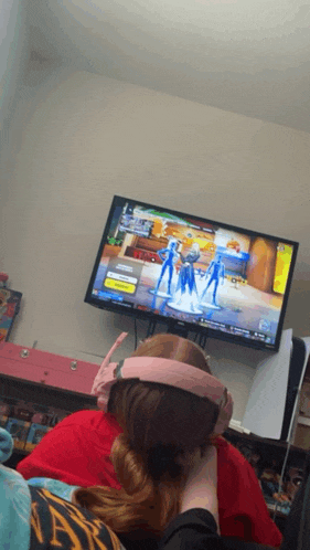 a girl wearing pink headphones watches a video game on a flat screen tv