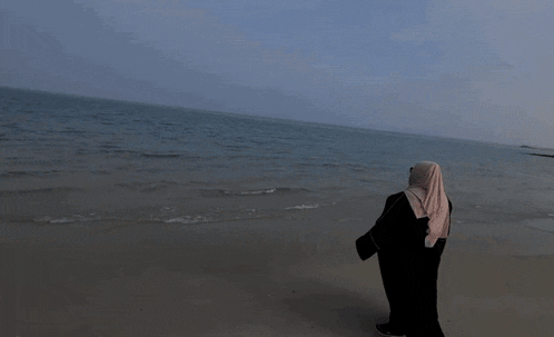 a woman wearing sunglasses and a hijab stands on the beach