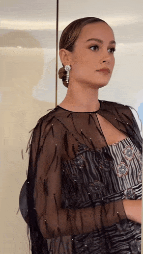 a woman wearing a black dress and earrings is standing in front of a white wall