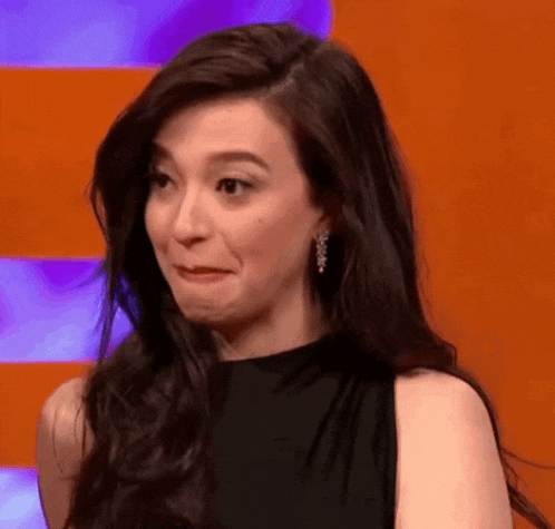 a woman with long dark hair is making a funny face while wearing a black dress and earrings .