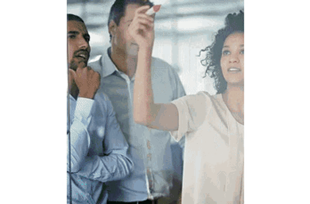 a group of people are standing around a glass wall while a woman throws a dart at it .