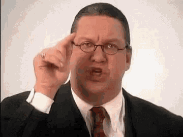 a man in a suit and tie is making a funny face and pointing at his forehead .
