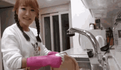 a woman is washing dishes in a kitchen sink wearing pink gloves .