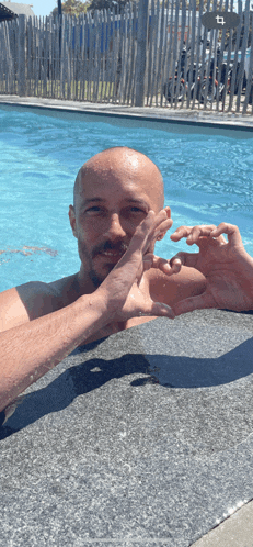 a man making a heart shape with his hands in a pool