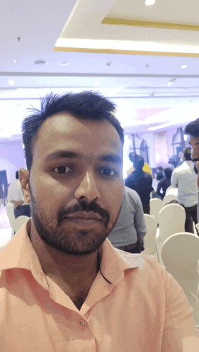 a man with a beard wearing a pink shirt is taking a selfie