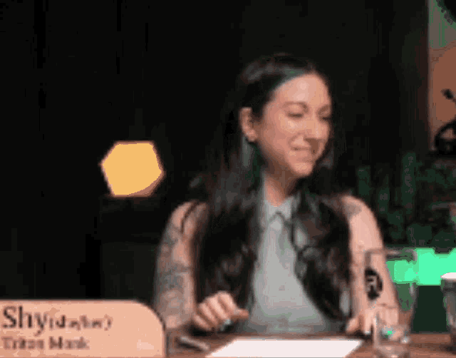 a woman with green hair is sitting at a table with a sign that says ' shydaly ' on it .