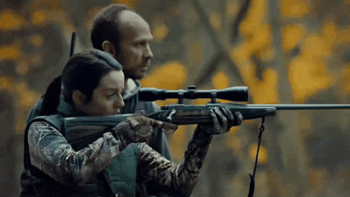 a man and a woman are holding guns in the woods