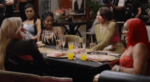 a group of women are sitting around a table with plates and glasses of wine .