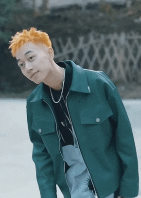a young man with orange hair wearing a green jacket