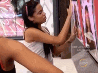 a woman in a white tank top is standing in front of a tv screen that says bad girls club on it