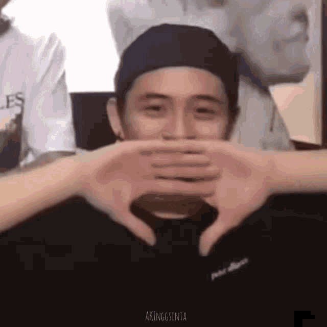 a man is making a heart shape with his hands while wearing a hat .