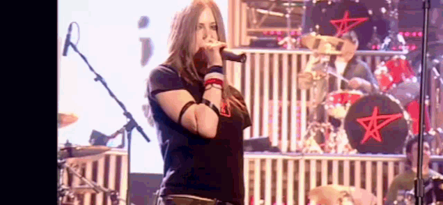 a woman is singing into a microphone on a stage with a drum set in the background .