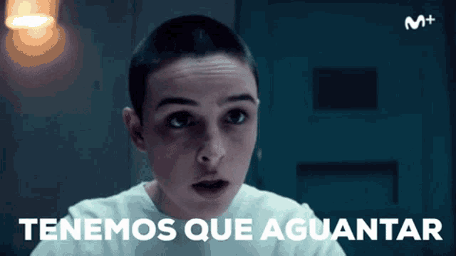 a woman with a shaved head is looking at the camera with the words tenemos que aguantar behind her