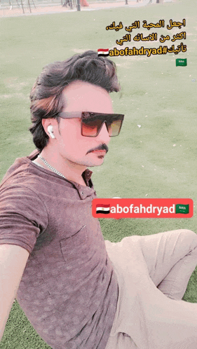a man wearing sunglasses sits on a grassy field with the name abofahdryad on the bottom