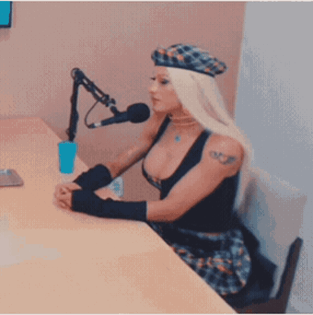 a woman wearing a beret sits at a table with a microphone in front of her