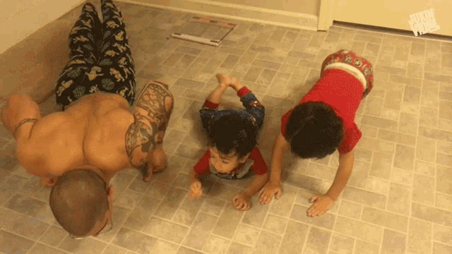 a man and two children are doing push ups on a tiled floor with a jukin video watermark in the corner