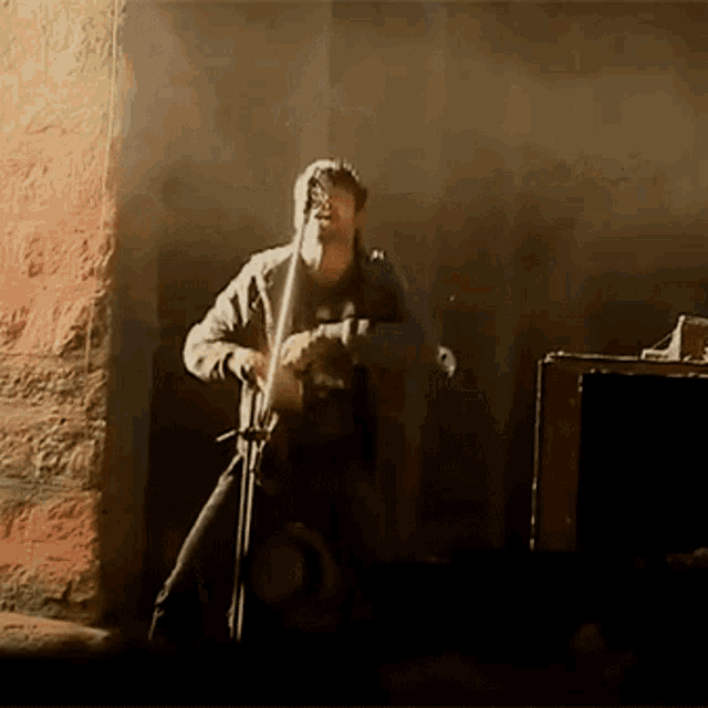 a man playing a guitar in a dark room with a brick wall in the background
