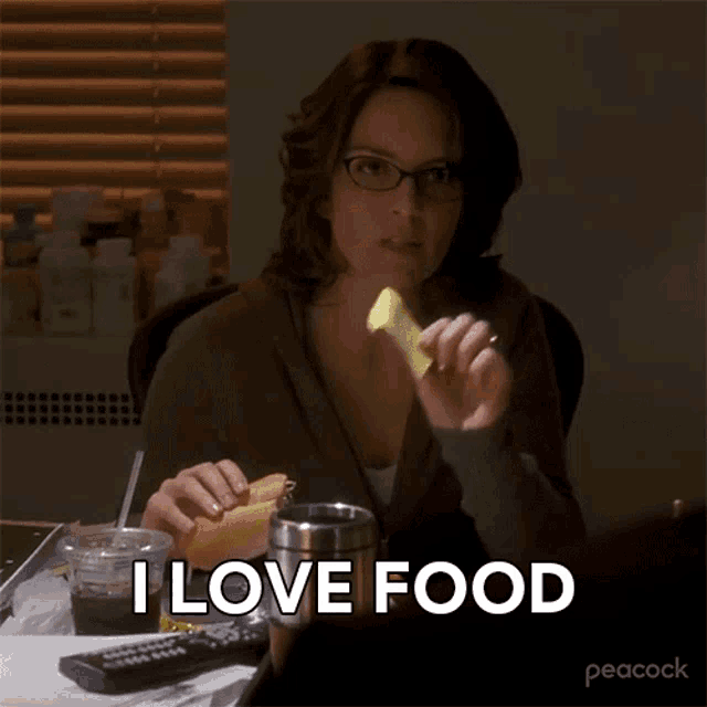 a woman is sitting at a table with a sandwich and a cup of coffee and says i love food