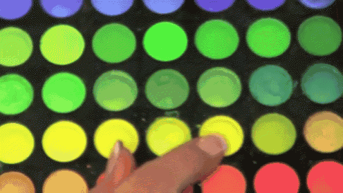 a person 's hand is touching a yellow circle in the middle of a rainbow of circles
