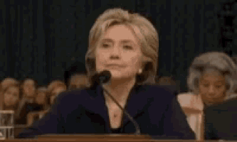 hillary clinton is giving a speech in front of a crowd while sitting at a podium .