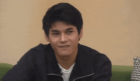 a young man in a black jacket is sitting on a green couch and making a funny face .