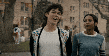 a man and a woman are walking down a sidewalk and the man is wearing a cardigan with the letter g on it