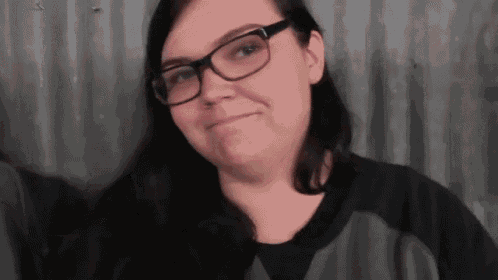 a woman wearing glasses and a gray shirt is smiling .
