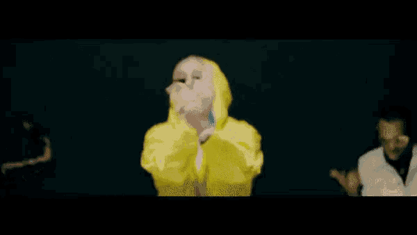 a blurry picture of a person wearing a yellow hoodie and giving the middle finger .