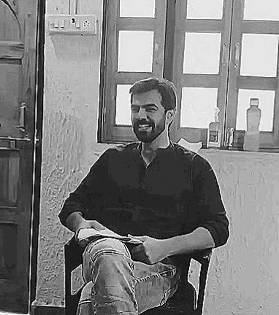 a man with a beard is sitting in a chair reading a book .